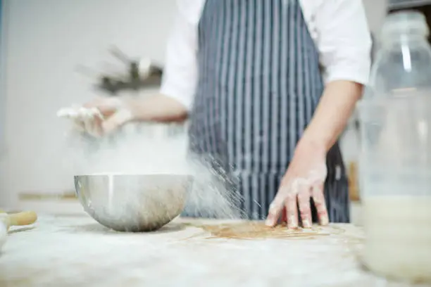 Chef in uniform sprinkling wheaten flour over workplace