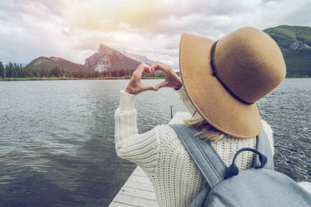 istock Young woman making heart shape finger frame on mountain lake 827536806