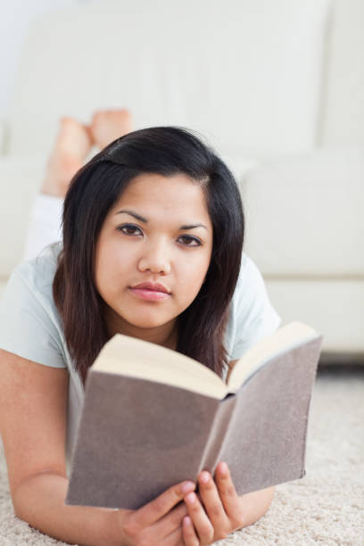 istock Woman holding a book while lying on the floor 827555006