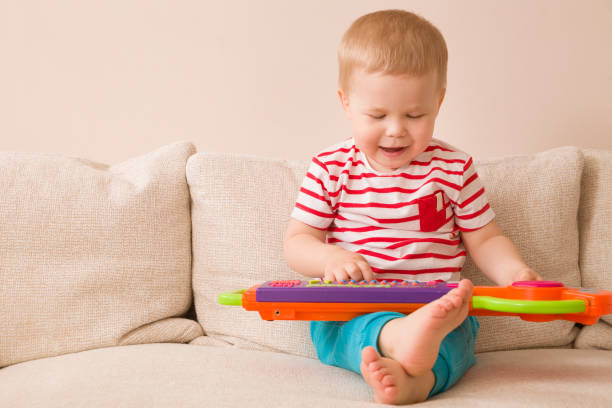 porträt von liebenswert kleinkind jungen auf dem sofa sitzen und spielen spielzeug-klavier. frühes lernen zu hause. kleine musiker. kinder und spielzeug. bildung. im innenbereich. - babies only audio stock-fotos und bilder