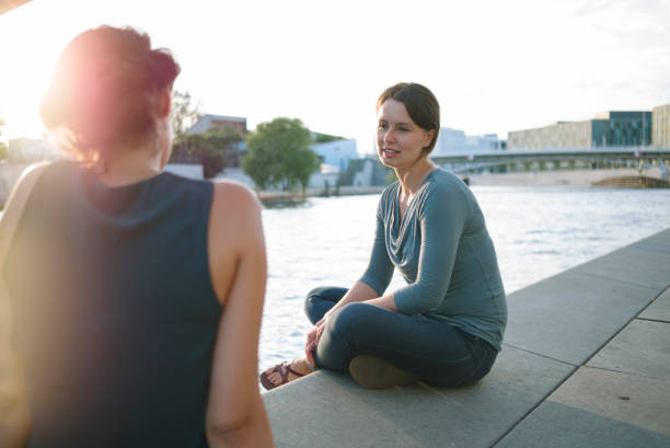 friendship: two young woman talking, river in background, summer