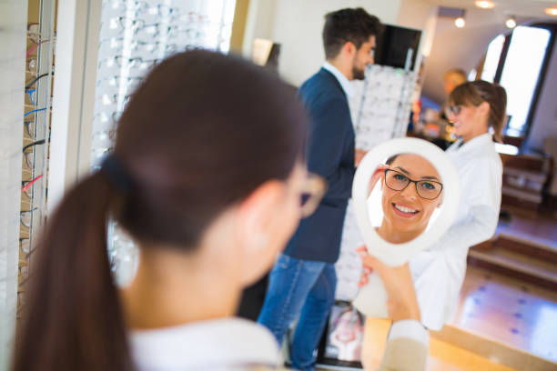istock Woman choosing glasses in optical store using mirror 827562206