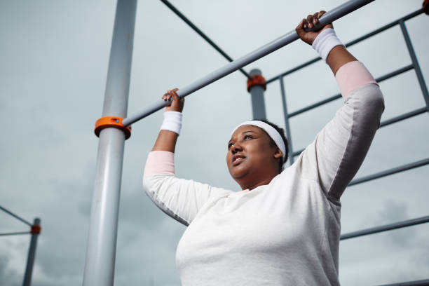 Determined overweight African woman practicing pull-up exercise outdoors Determined overweight African woman practicing pull-up exercise outdoors chin ups photos stock pictures, royalty-free photos & images