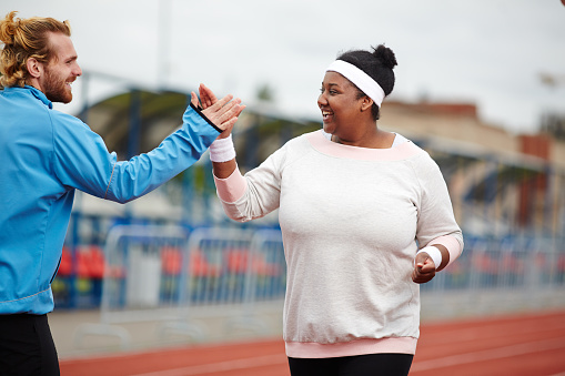 Happy plus-size woman giving high five to her personal trainer while running on track