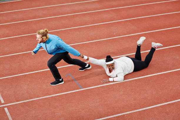 Determined personal trainer dragging exhausted overweight woman on track motivating her to keep running Determined personal trainer dragging exhausted overweight woman on track motivating her to keep running dragging photos stock pictures, royalty-free photos & images