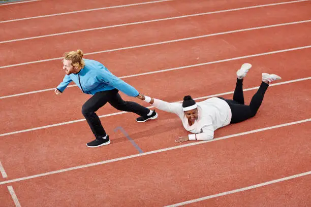 Photo of Determined personal trainer dragging exhausted overweight woman on track motivating her to keep running