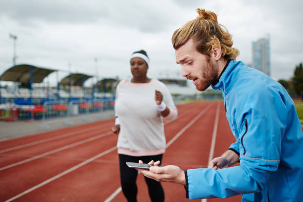 istock Personal trainer measuring time on smartphone while overweight female client running on track 827571580