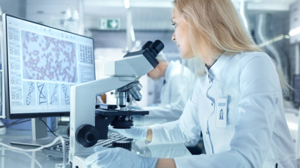 female research scientist using electronic microscope. she and her colleagues work in a big modern laboratory/ medical centre. - smiling research science and technology clothing imagens e fotografias de stock