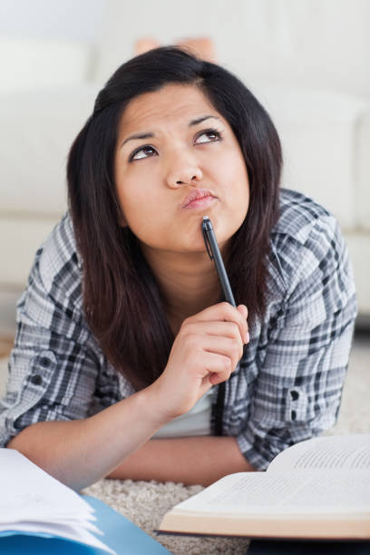 istock Thinking woman laying on the floor while holding a pen with a book 827576166