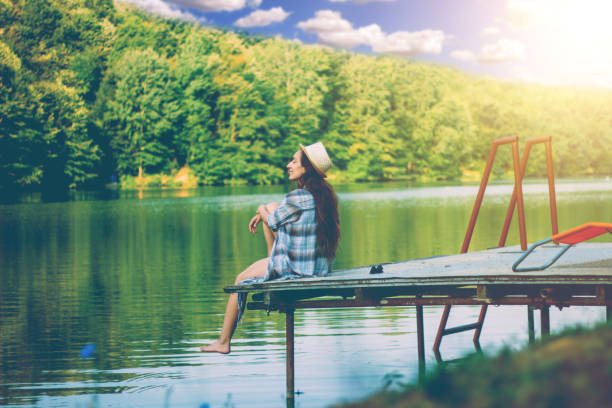 istock Girl sitting on pier and lookingat the river 827580842