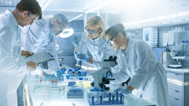 istock Team of Medical Research Scientists Work on a New Generation Disease Cure. They use Microscope, Test Tubes, Micropipette and Writing Down Analysis Results. Laboratory Looks Busy, Bright and Modern. 827580984