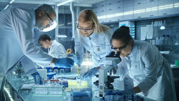 Team of Medical Research Scientists Work on a New Generation Disease Cure. They use Microscope, Test Tubes, Micropipette and Writing Down Analysis Results. Laboratory Looks Busy, Bright and Modern. trabajo en equipo de científicos de la investigación médica en la curación de una enfermedad de nueva generación. utilizan microscopio, tubos de ensayo, micropipetas y escrito por análisis de resultados. laboratorio se ve ocupada, luminoso y moderno.