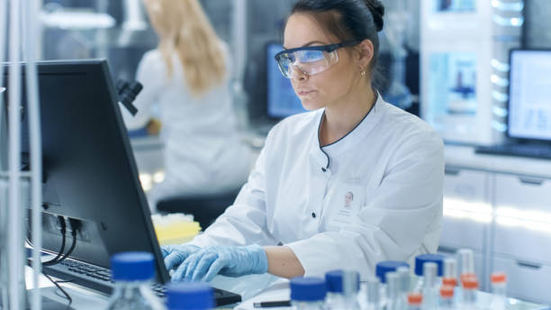 medical research scientist typing information obtained from new experimental drug trial. she works in a bright and modern laboratory. - smiling research science and technology clothing imagens e fotografias de stock