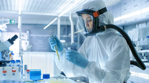 científico de investigación de virología médica trabaja con máscara, un traje de materiales peligrosos, utiliza una micropipeta. ella trabaja en un laboratorio estéril alta tecnología, centro de investigación. - traje protector fotografías e imágenes de stock