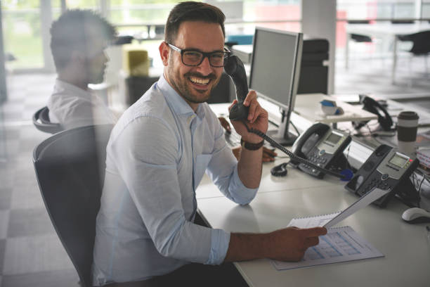 homme d’affaires caucasien ayant conversation sur téléphone fixe. homme d’affaires au bureau. regardant la caméra. - dispatcheur photos et images de collection