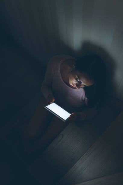istock Woman sitting on steps while checking a digital tablet in the darkness 827595860