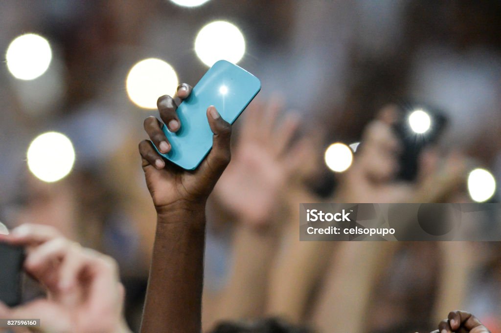 Mobile in the hand of spectators Person holding a cellphone with the flash on and hands up Mobile Phone Stock Photo