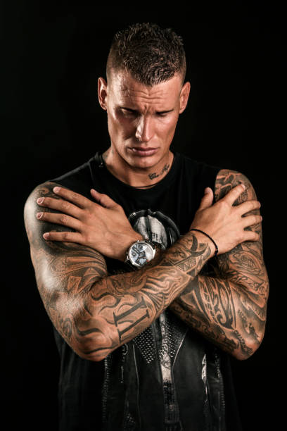 Young man with tatoos posing in studio on black background. About 25 years old, Caucasian male.