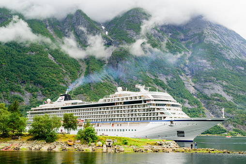 Eidfjord: Travel documentary of the luxury cruise ships Viking Star moored in fjord. High and steep mountainside in background with rainclouds in the sky.