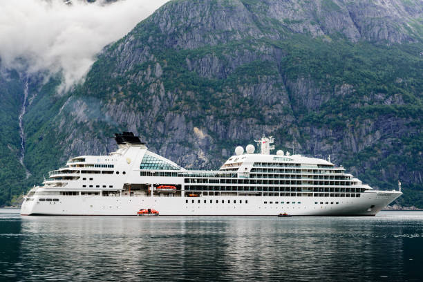 Eidfjord: Travel documentary of the luxury cruise ship Seaborn Quest moored in fjord. High and steep mountainside in background with rainclouds in the sky.