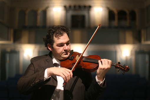 Violinist playing violin in a music theatre. About 35 years old, Caucasian male in formalwear.