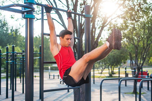 Fitnes man hanging on wall bars performing legs raises. Core cross training working out abs muscles.