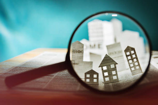 Paper house under a magnifying lens Magnifying glass in front of an open newspaper with paper houses. Concept of rent, search, purchase real estate. military private stock pictures, royalty-free photos & images