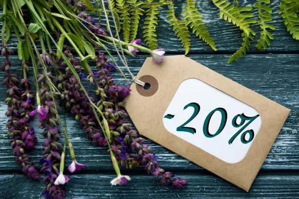 Discount label tag with an inscription "-20%" and a Wild Red flowers blossom and green leaves on the black rustic wooden table background.Final Sale poster, banner or summer sale concept.