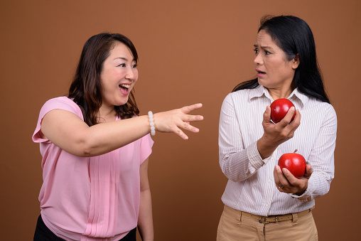 Studio shot of two mature Asian businesswomen together as friends against colored background horizontal shot