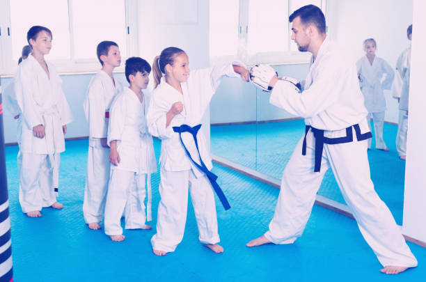 istock Children training karate kicks on punching bag during karate class 827623604