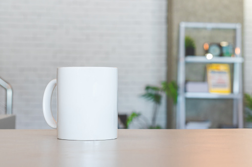 White mug on table and modern room background. Blank drink cup for your design. Can put text, image, and logo.