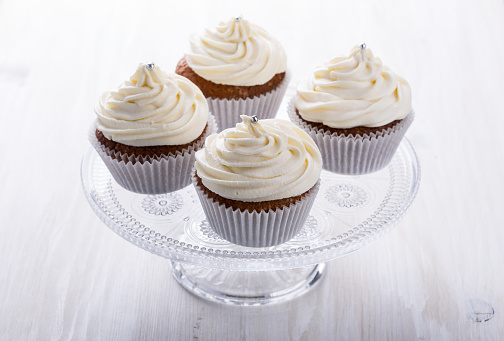 Homemade cupcakes with creamcheese frosting on cake stand on light background