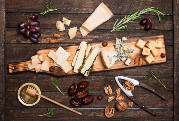 istock Cheese platter with different cheeses, grapes, nuts, honey, bread and dates on rustic wooden background. Retro styled cheese variety selection on dark wood board. 827643314