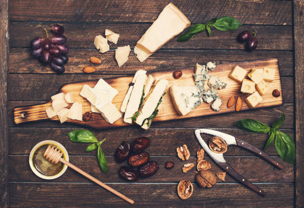 istock Cheese platter with different cheeses, grapes, nuts, honey and dates on rustic wooden background. Retro styled cheese variety selection on wood board. 827646168