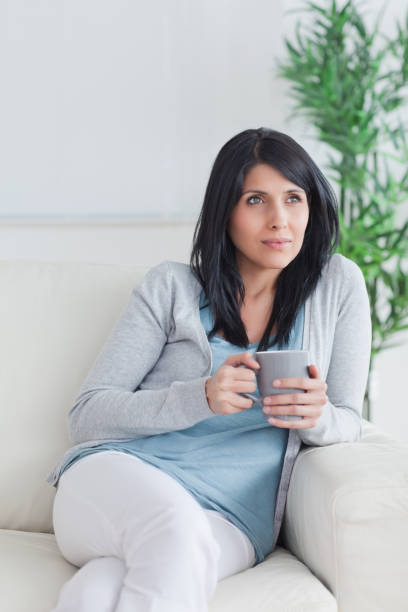 istock Woman sitting on a couch while crossing her legs and holding a mug 827646414