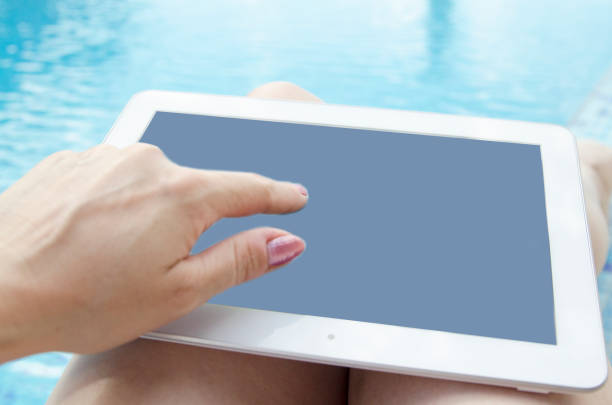 istock Woman hand using mock up digital tablet black screen on pool side.Summer vacation and internet communication concept. Necessary technology for business far from home. 827646598