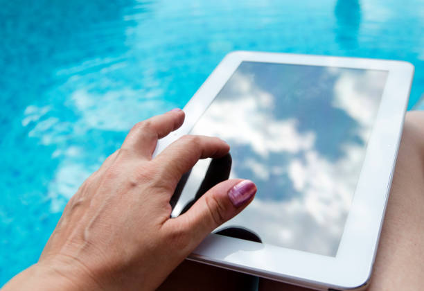 istock Woman hand using mock up digital tablet black screen on pool side.Summer vacation and internet communication concept. Necessary technology for business far from home. 827647082