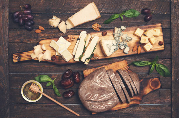 istock Cheese platter with different cheeses, grapes, nuts, honey, bread and dates on rustic wooden background. Retro styled cheese variety selection on wood board. 827647278