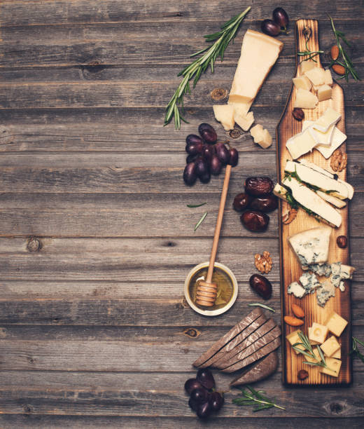 Cheese selection on wooden rustic board. Cheese platter with different cheeses, grapes, nuts, honey and dates on weathered wood background.