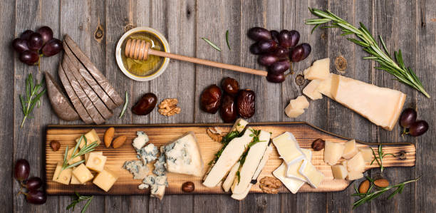 istock Cheese selection on wooden rustic board. Cheese platter with different cheeses, grapes, nuts, honey and dates on weathered wood background. 827649866