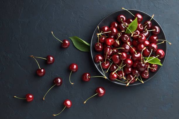 ciliegia dolce fresca in piatto nero su sfondo di pietra blu scuro. - black cherries foto e immagini stock