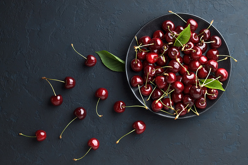 Fresh sweet cherry in black plate on dark blue stone background. Summer delicious berry. Top view with copy space.