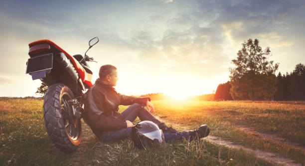 Man having rest in the countryside during motorbike trip Man relaxing during sunset in countryside with his motorbike. See the note please. motorcycle biker stock pictures, royalty-free photos & images