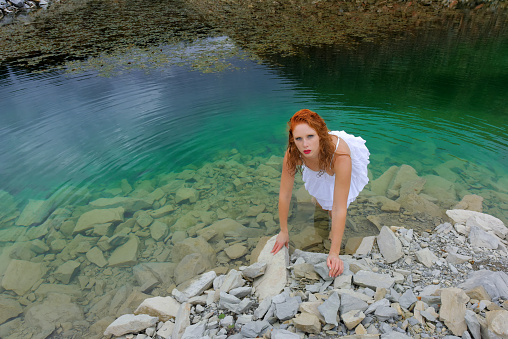 A young red headed girl poses in the green water of a stone quarry.