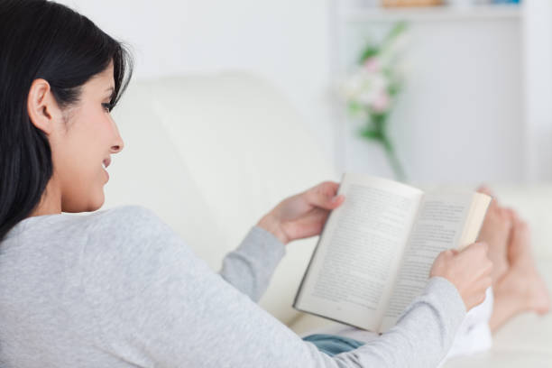 istock Woman reading a book while laying on a sofa 827680686