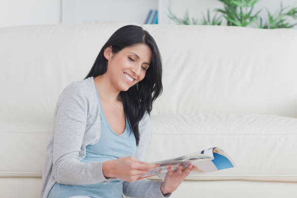 istock Smiling woman holding a magazine while sitting on the floor 827681190
