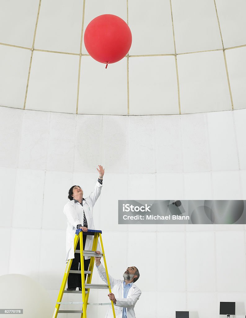 Scientist on ladder watches balloon float away  Scientist Stock Photo