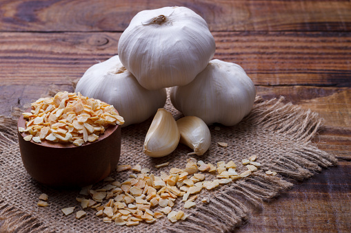 Stock photo showing close-up view of a stack of fresh, whole garlic bulbs on a mottled black plate, against a mottled black background.