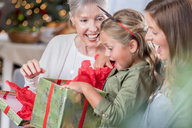 excited girl is surprised while opening christmas present - grandmother giving gift child imagens e fotografias de stock