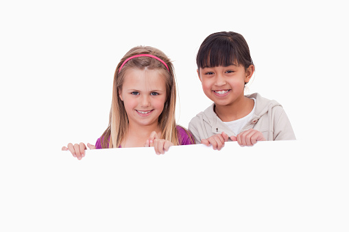 Girls behind a blank panel against a white background